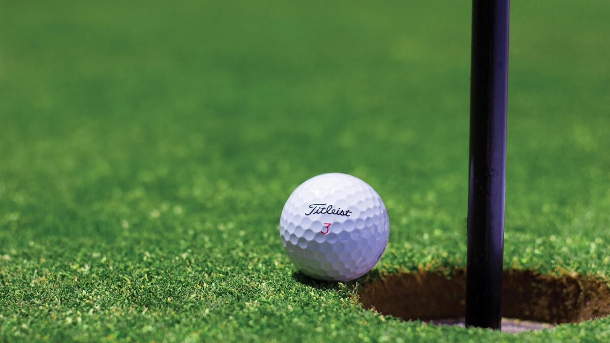Balle de golf blanche marquée « Titleist » et du chiffre 3, posée sur un green herbeux près d'un trou avec un drapeau noir.