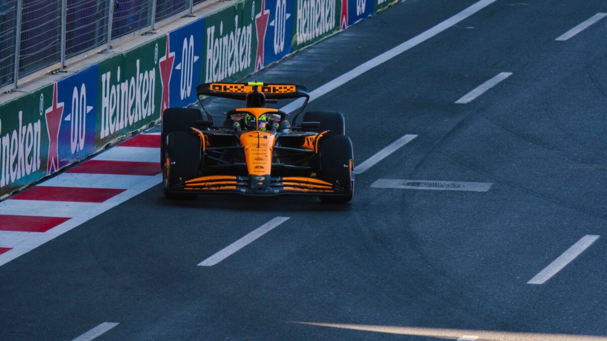 Une monoplace McLaren orange roulant sur un circuit urbain, longeant des barrières de protection publicitaires Heineken, avec une bordure rouge et blanche sur un asphalte sombre.