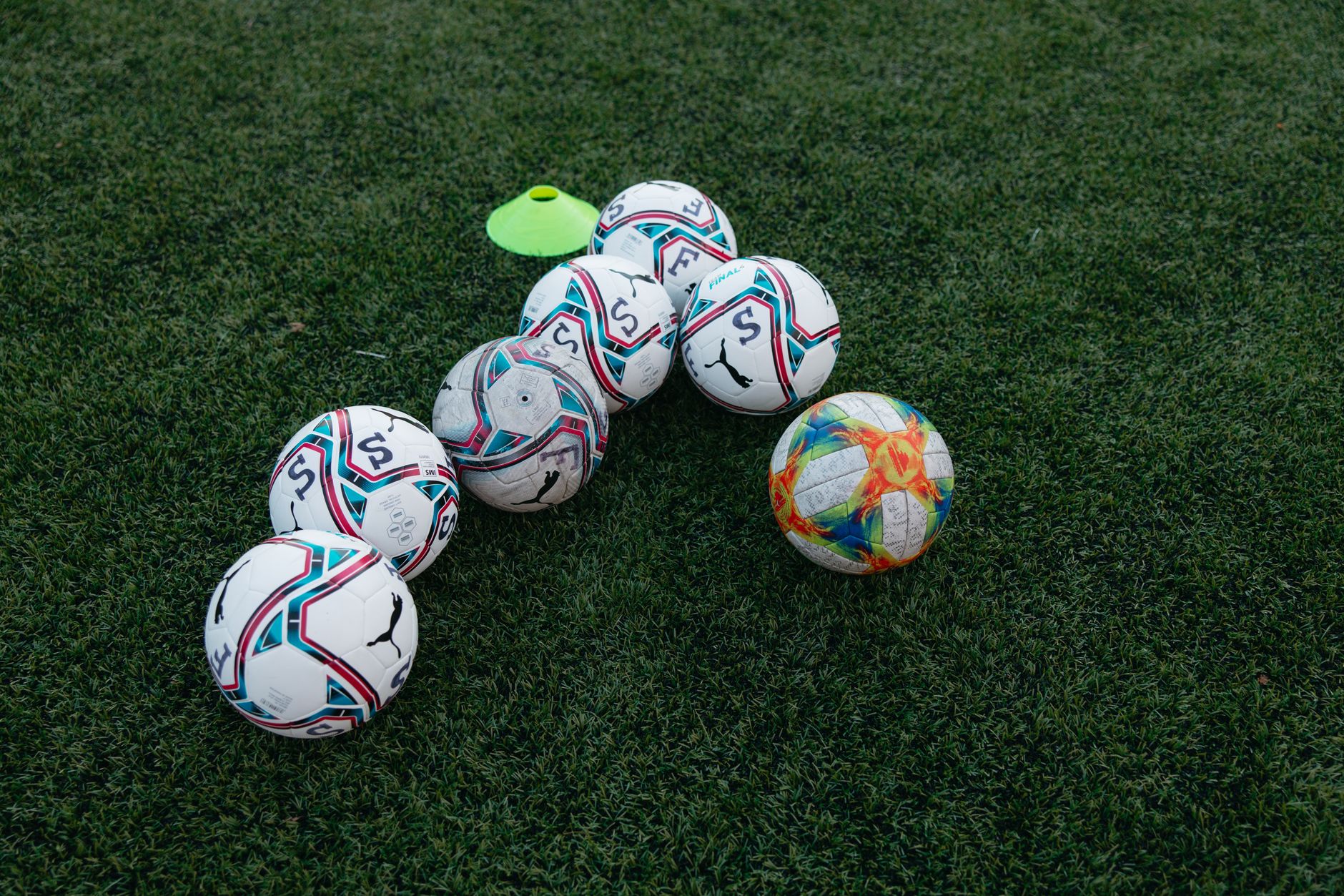 A soccer ball and training cones placed on a grass pitch