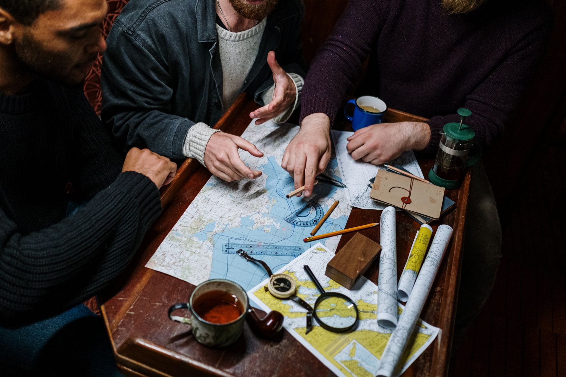 People studying paper maps and navigation tools laid out on a wooden table.